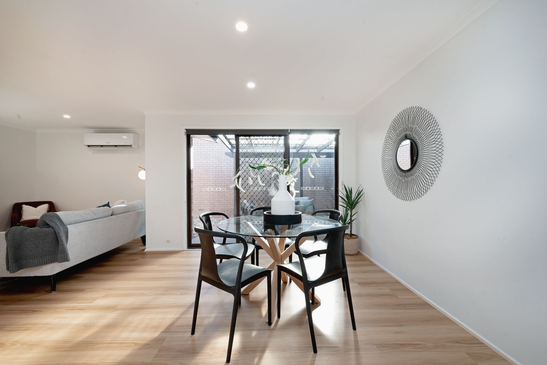 Dining room with glass table, black chairs, and white walls, with sliding doors to a patio.