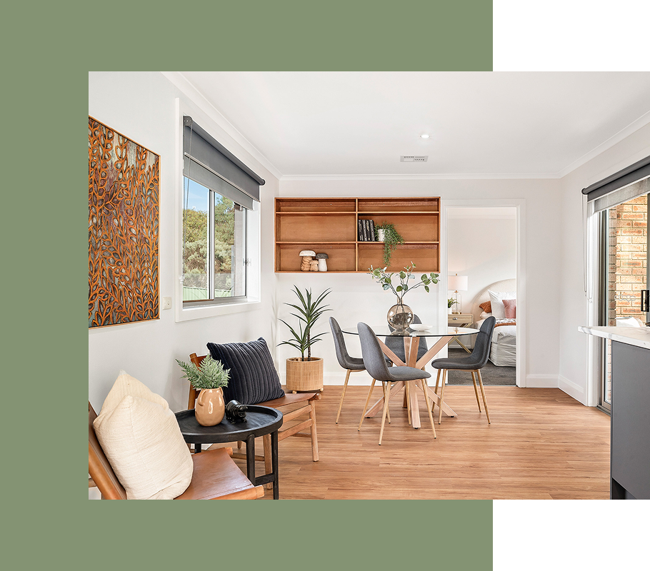 Dining room with wooden floor, table, chairs, shelving, and a view into a bedroom.