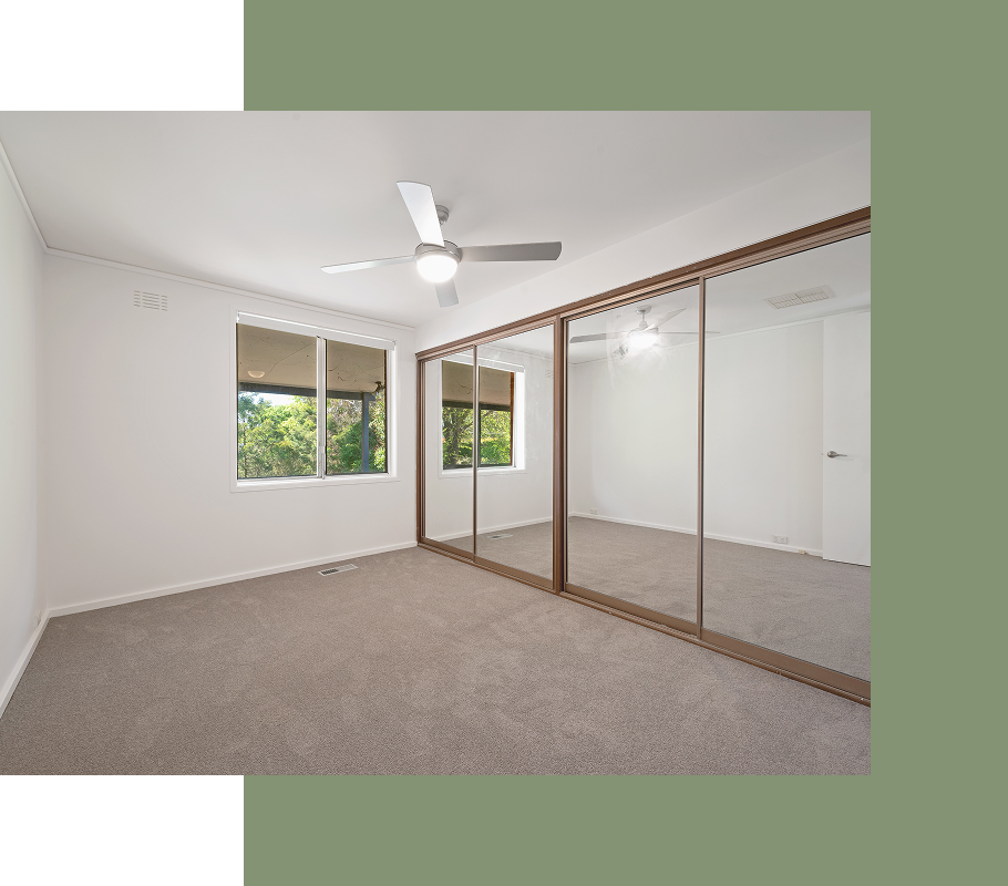 Bedroom with large mirrored closet doors, windows, ceiling fan, and beige carpet.