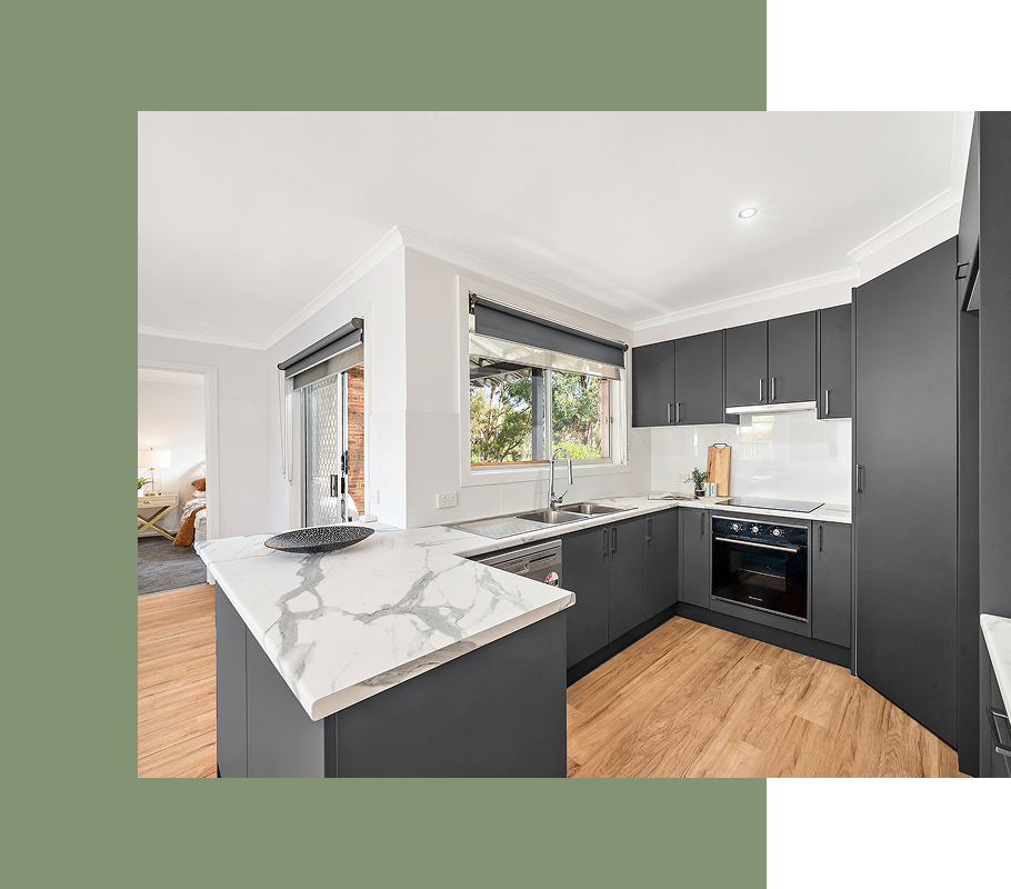 Modern kitchen with gray cabinets, marble countertops, and light wood flooring.