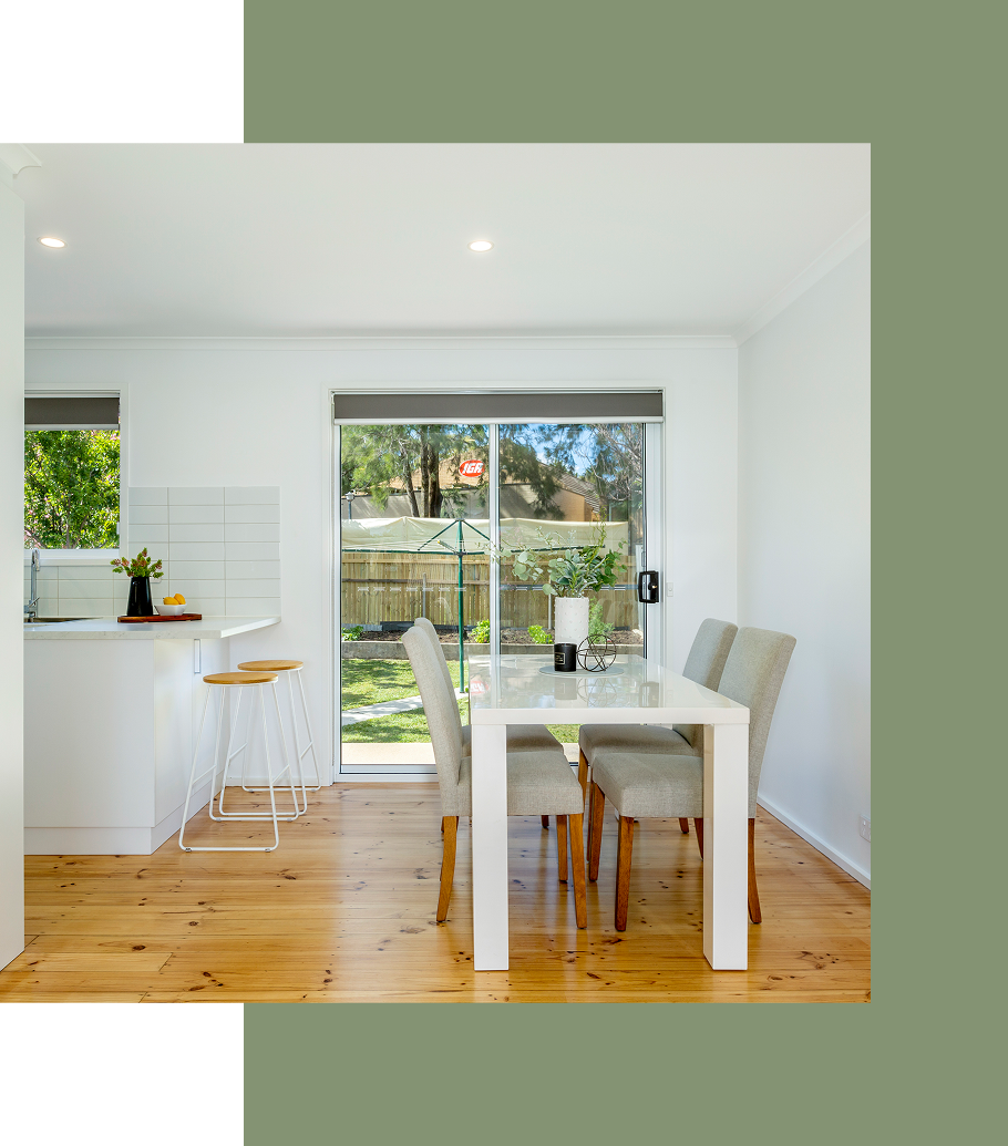 Dining room with white table and chairs, sliding glass door, wooden floors.