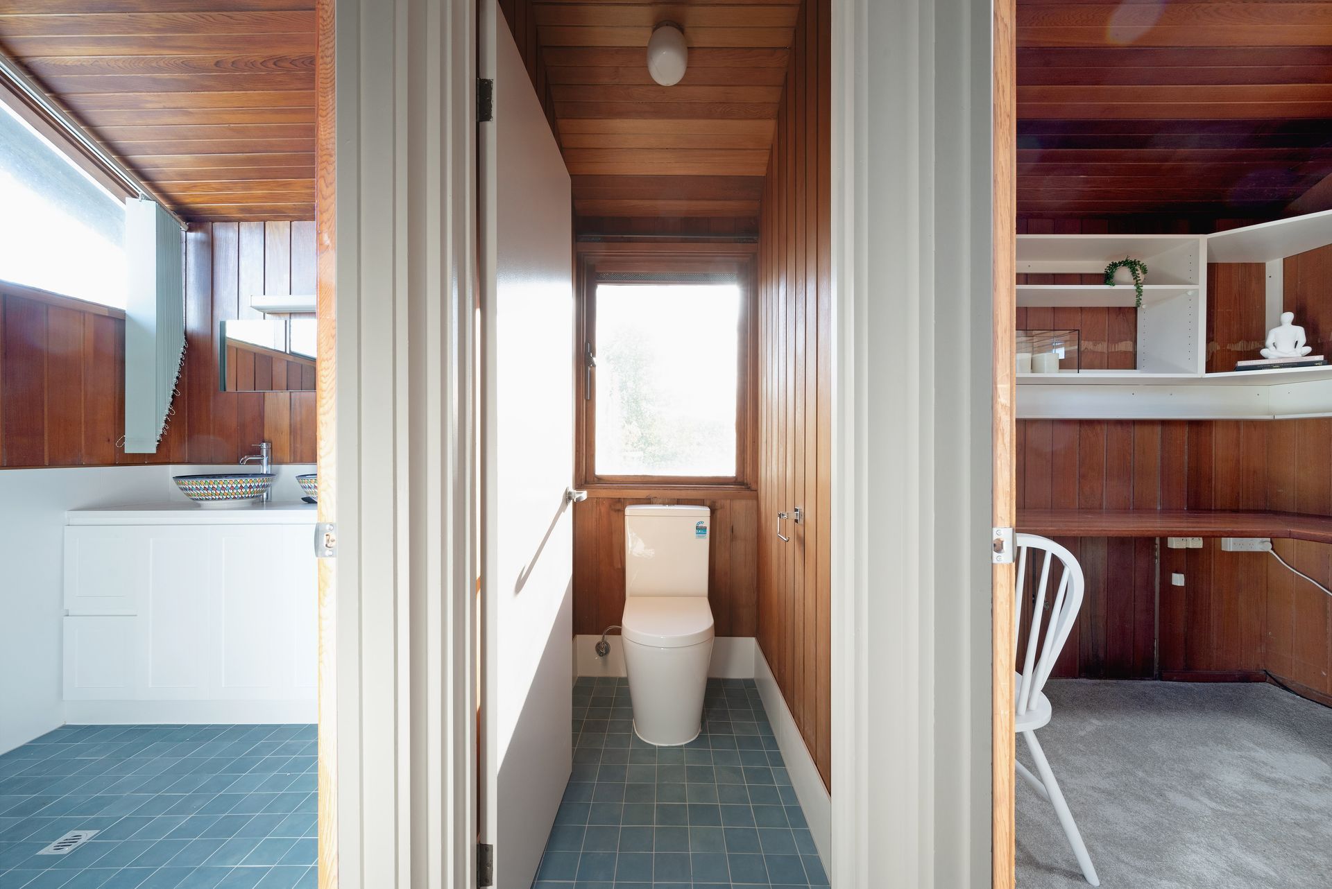 Interior view of a wooden-paneled bathroom with a toilet and a small window.