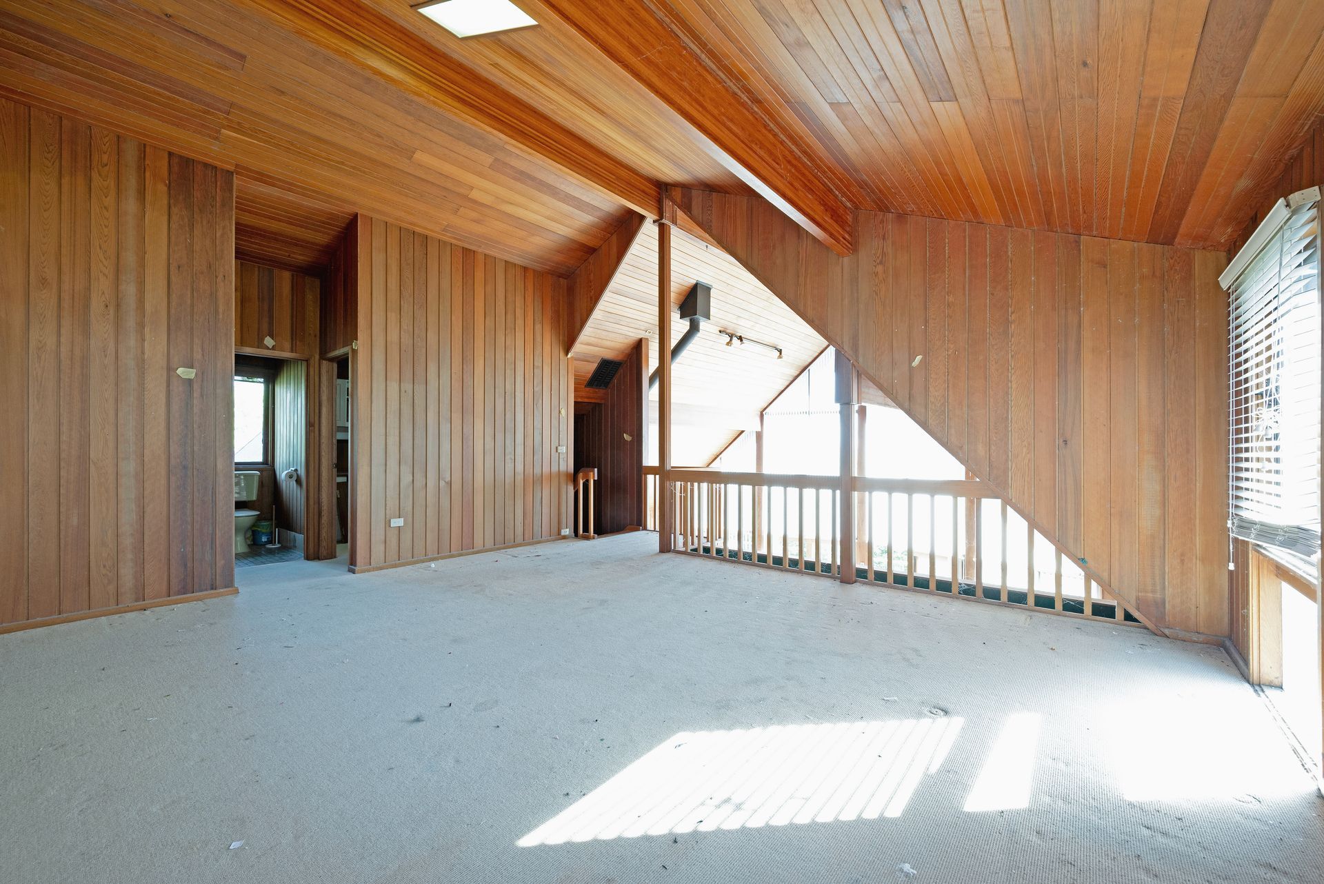 Empty room with wood paneling on walls and ceiling, carpeted floor, and large window.