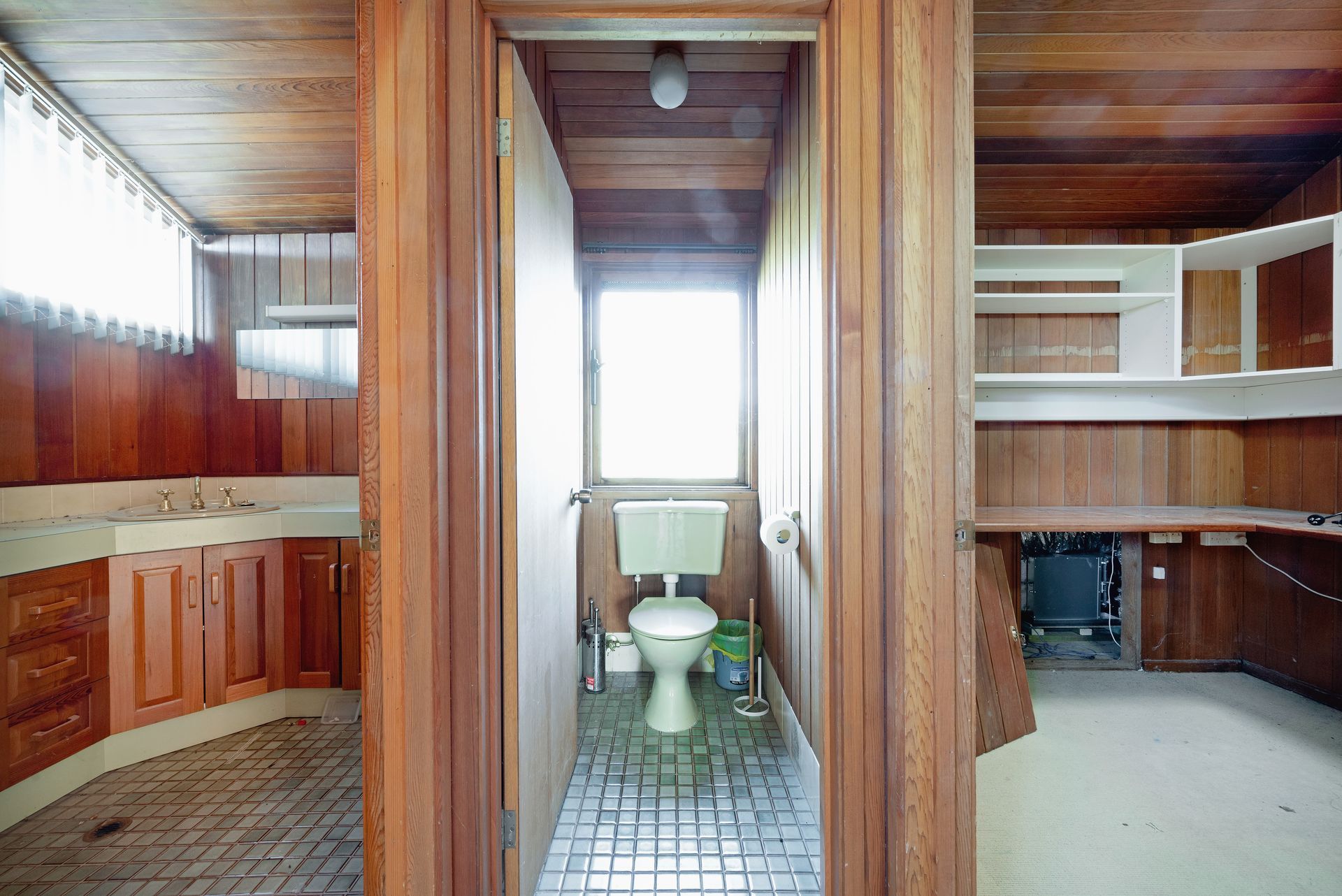 Wooden-paneled bathroom with a toilet, sink, and cabinetry; a window provides natural light.