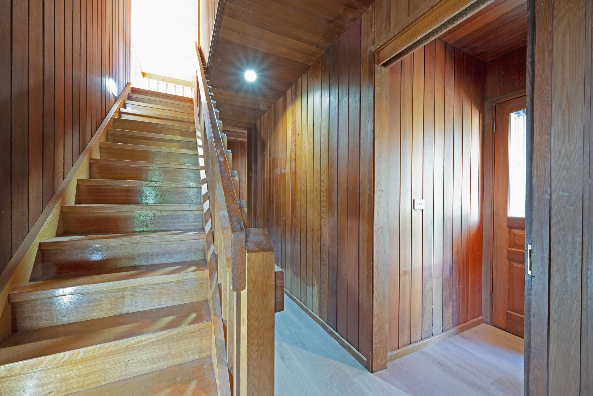 Empty room with wood paneling on walls and ceiling, two windows, and a metal step stool.