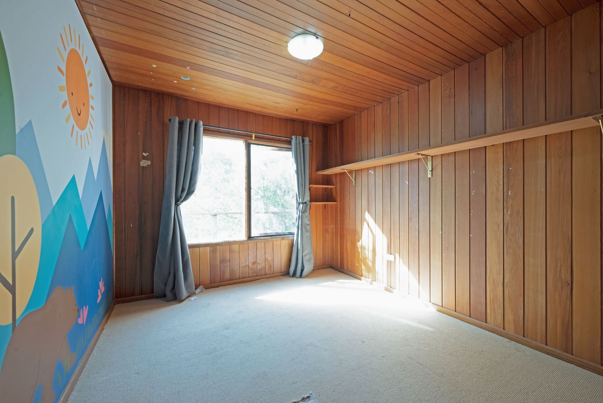Empty room with wood-paneled walls and ceiling, a window with curtains, built-in shelves, and carpet.