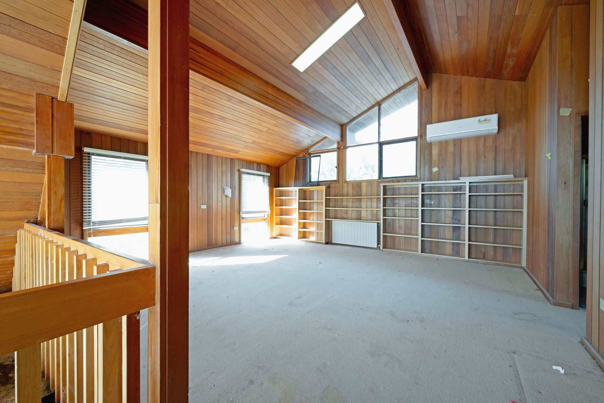 Empty room with wood paneling, sloped ceiling, built-in shelves, and a carpeted floor.