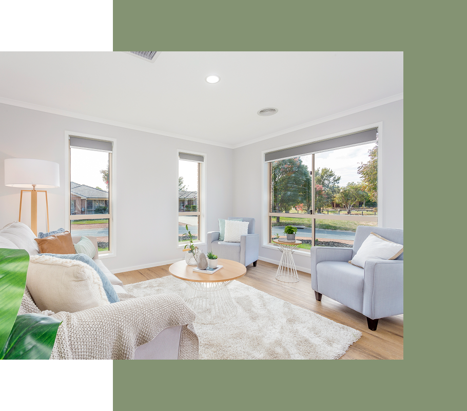 Living room with windows, light blue armchairs, and a shaggy rug, overlooking a green space.