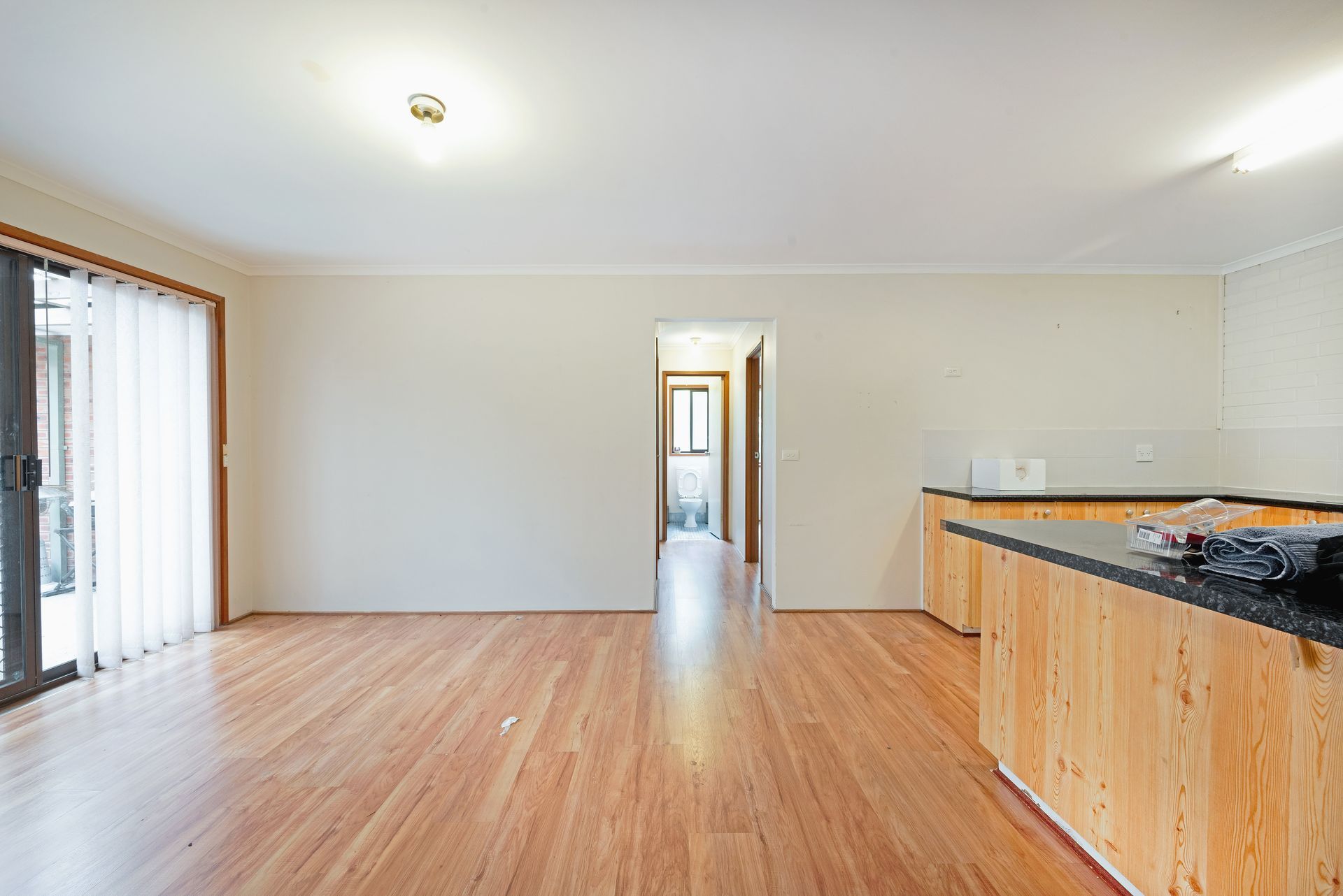 Empty kitchen with wooden cabinets, hardwood floor, and a sliding glass door.