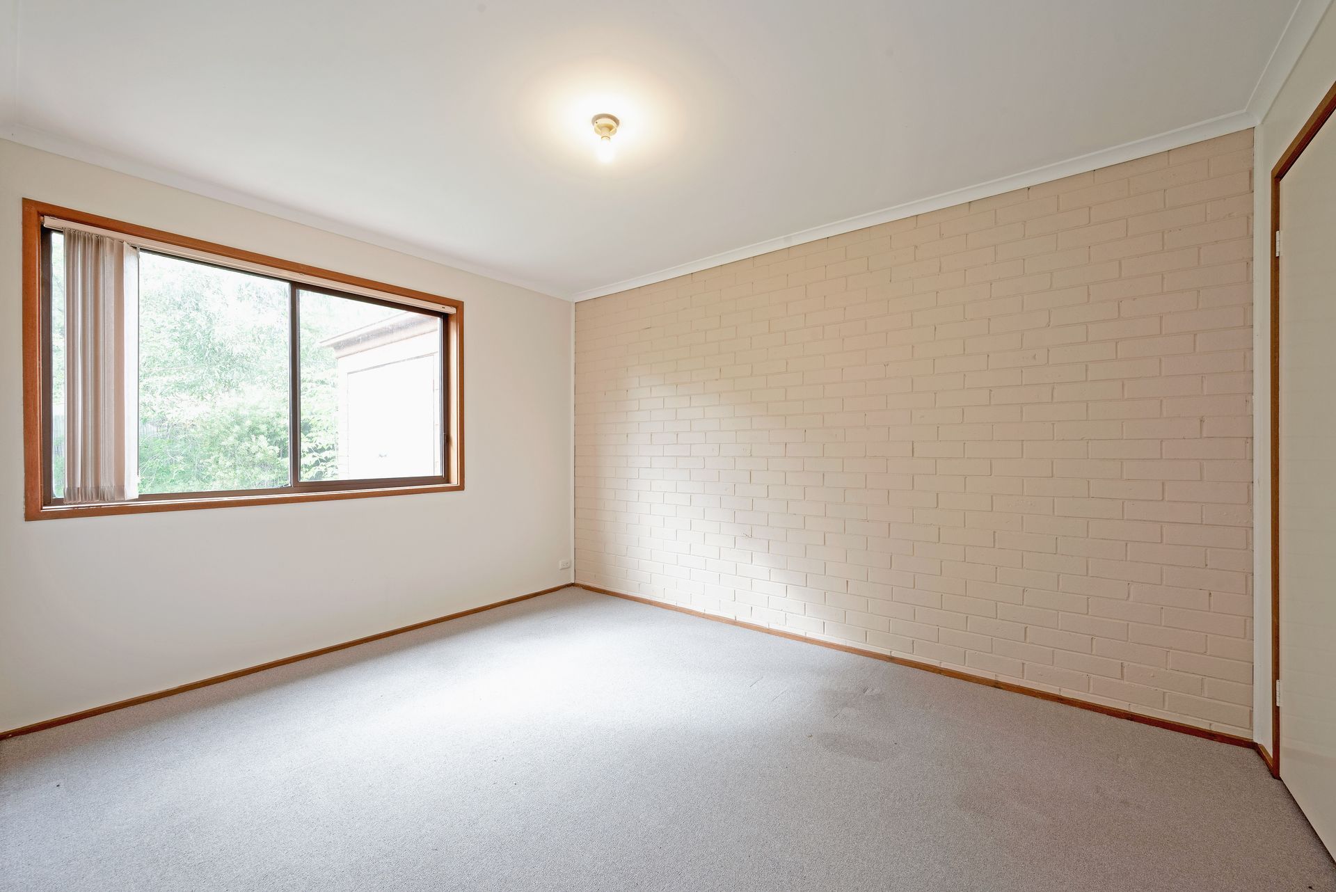 Empty room with window, brick wall, and carpet flooring.