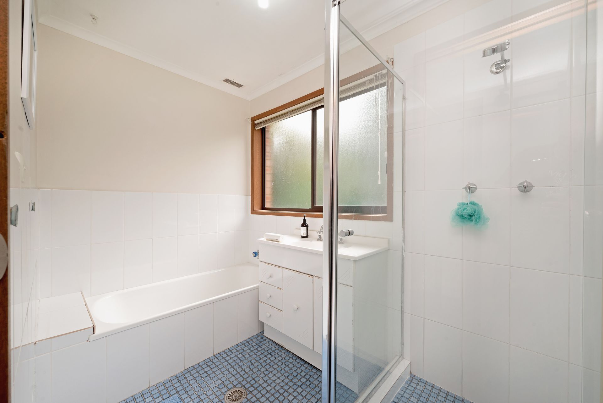 Bathroom with bathtub, shower, white tile, blue floor, and window with frosted glass.