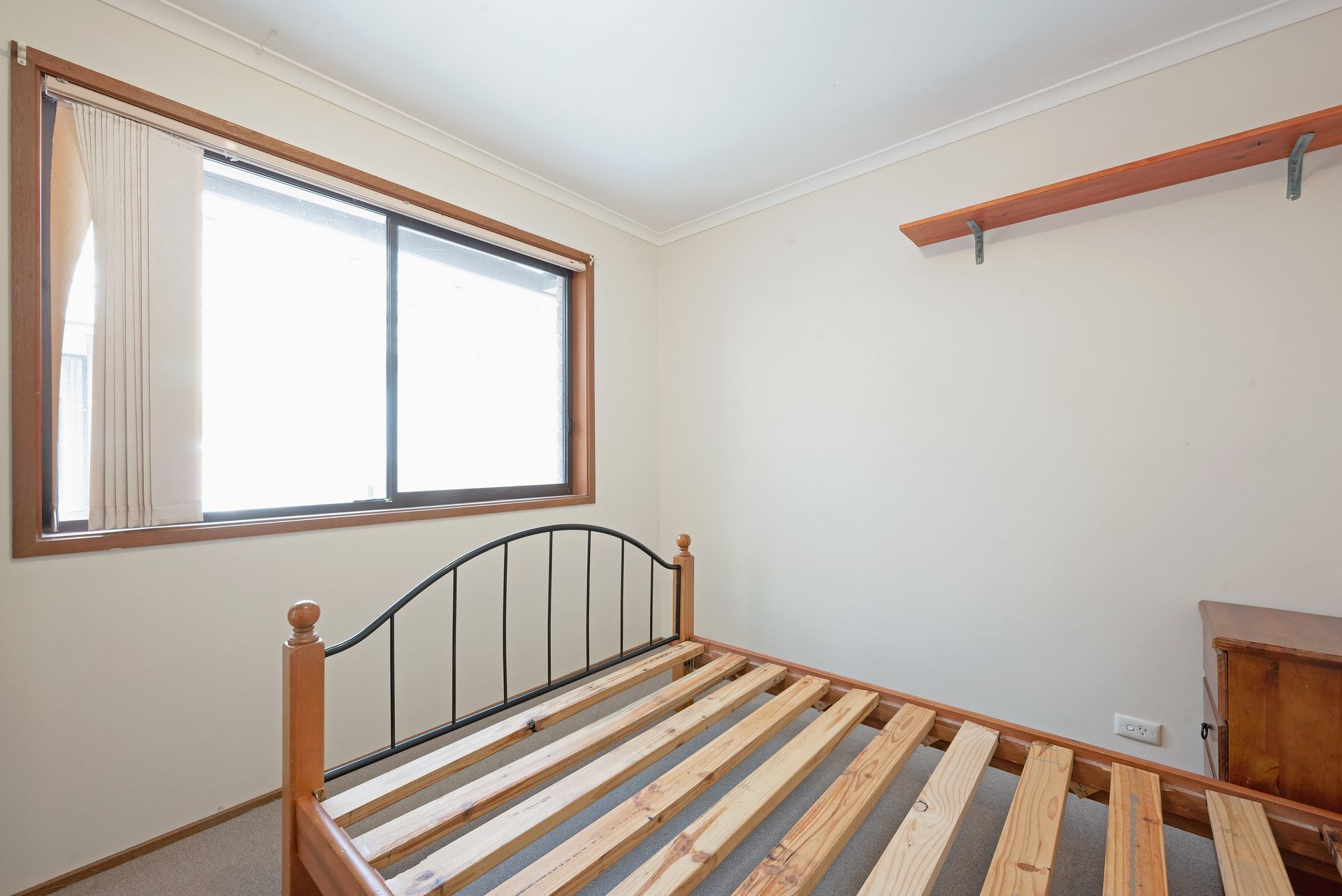 Bedroom interior with a bed frame, window with curtains, and wall-mounted shelf.