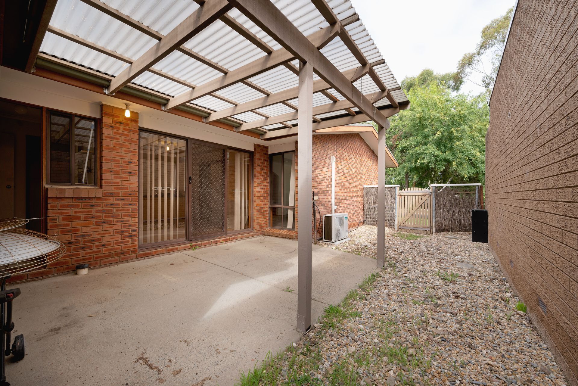 Patio area with a corrugated roof, brick walls, and gravel ground.