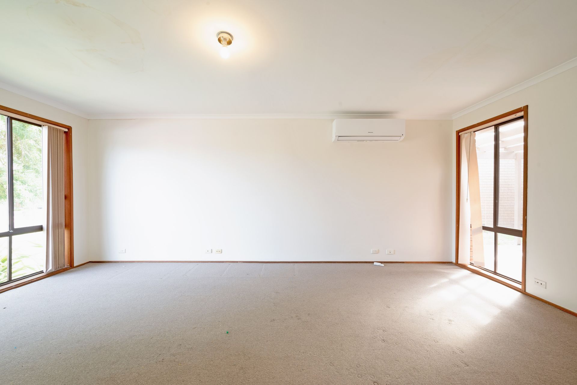 Empty room with beige carpet, light walls, two large windows, and an air conditioner.