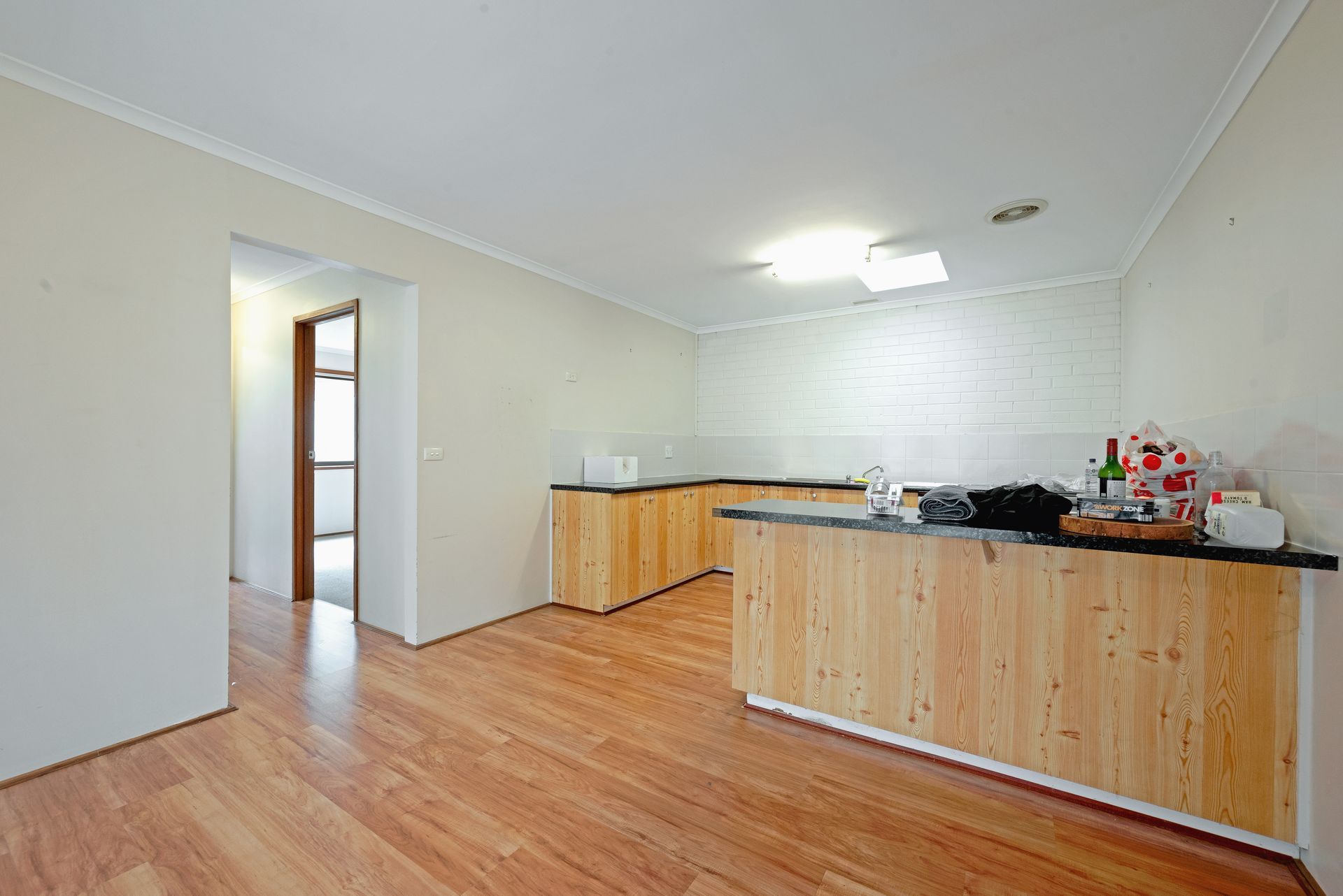 Empty kitchen with wood cabinets, brick backsplash, and a doorway to another room.