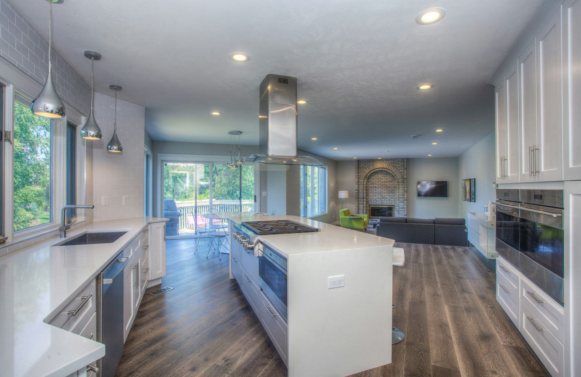 Modern kitchen with white cabinets, island with stovetop, and view of living room.