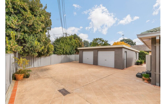 A concrete driveway leads to a gray garage with two doors, with trees and a cloudy sky in the background.