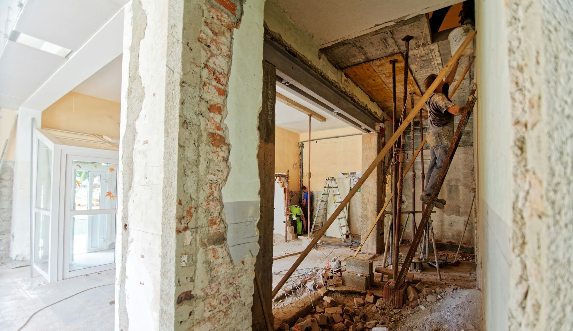 Interior demolition; workers inside a room with exposed brick and support beams.