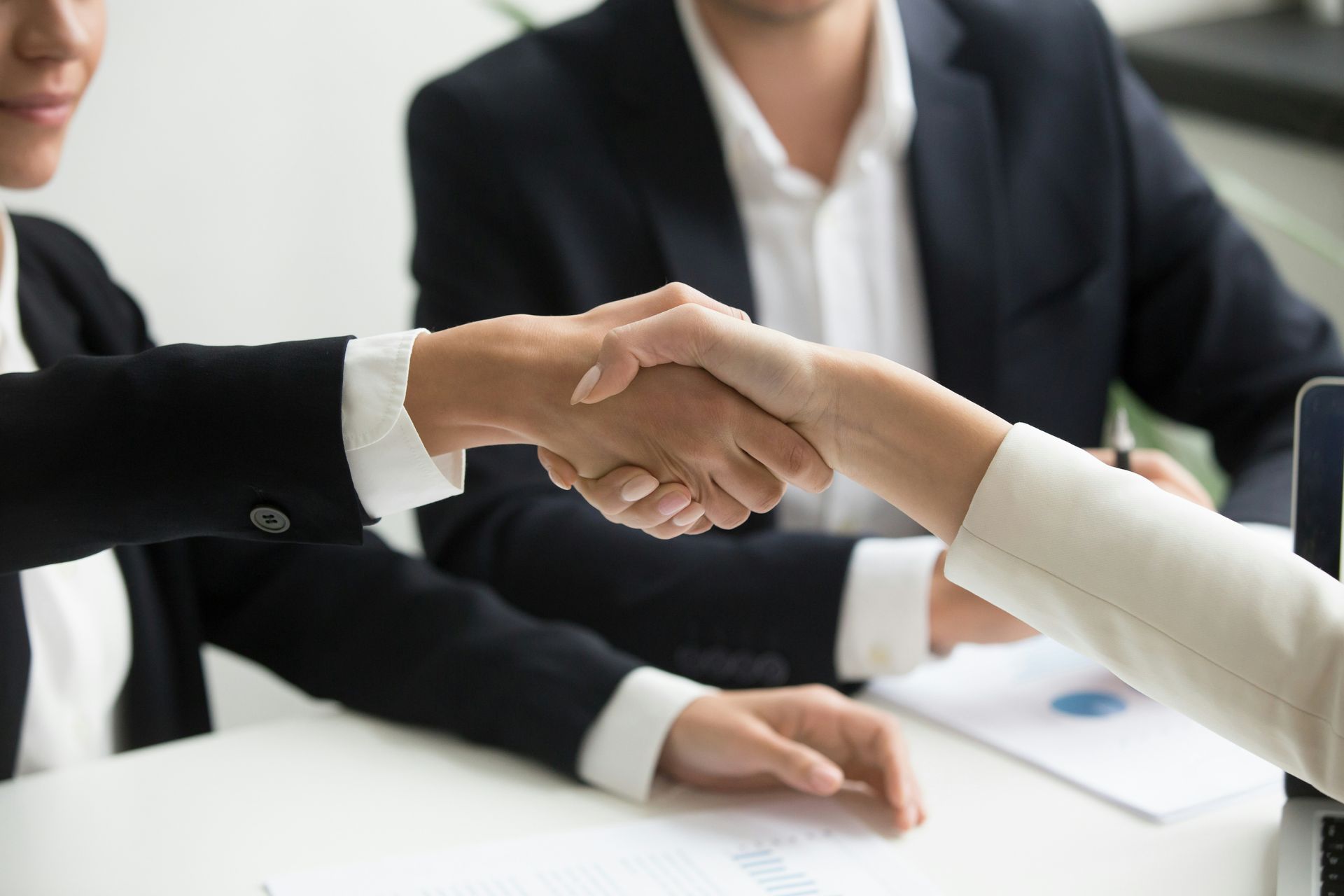 Two people in suits shaking hands over a table.