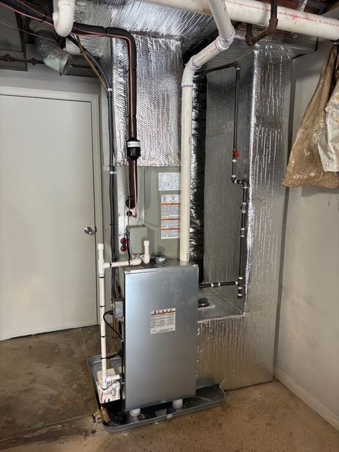 A metal furnace in a basement, pipes and ducts visible. Insulation and a closed door are also in view.