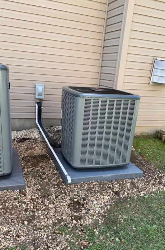 AC unit next to a house with pebble ground cover. Black piping leads to a white electrical box.