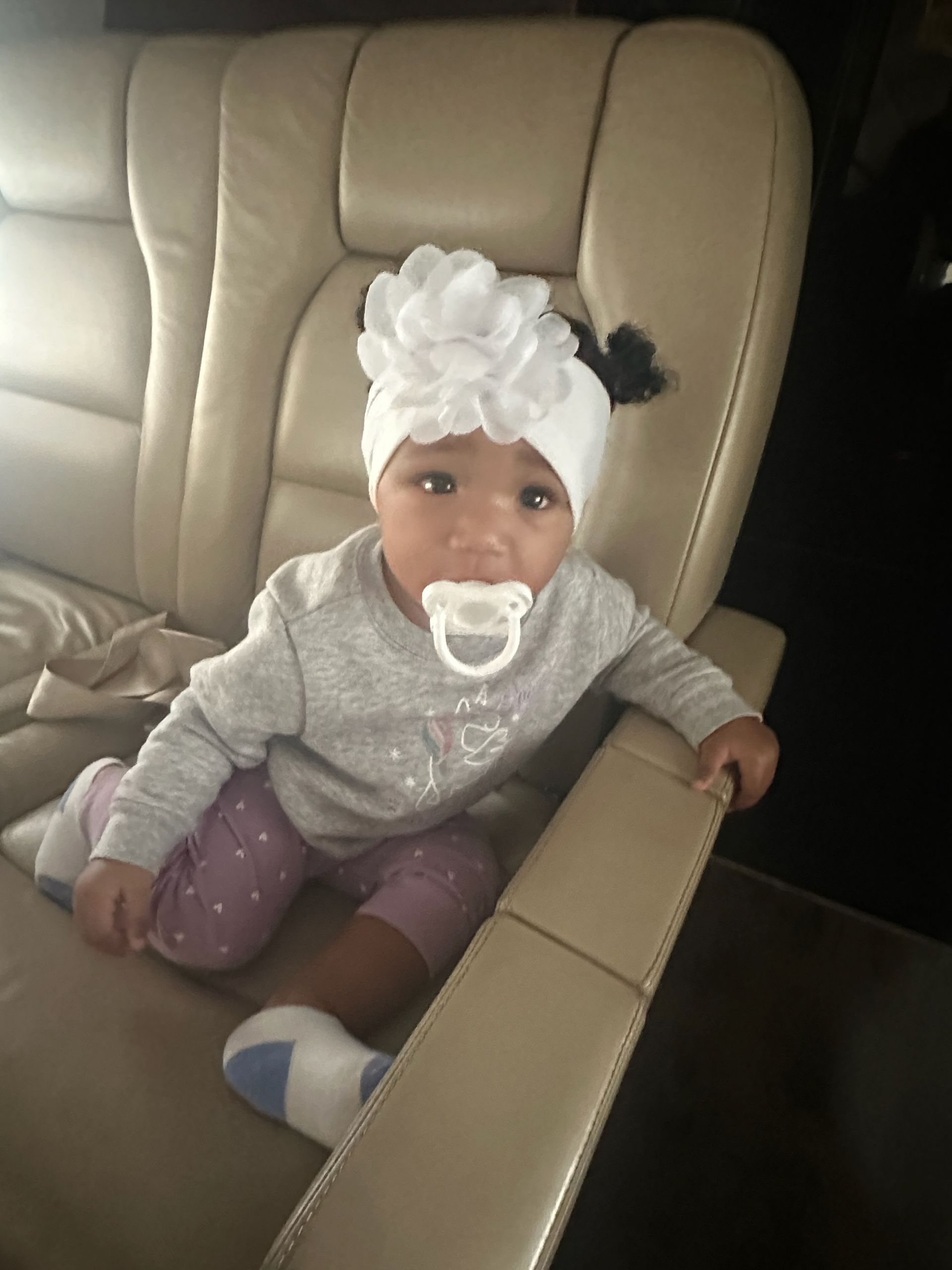 A baby is sitting in a chair with a pacifier in her mouth.