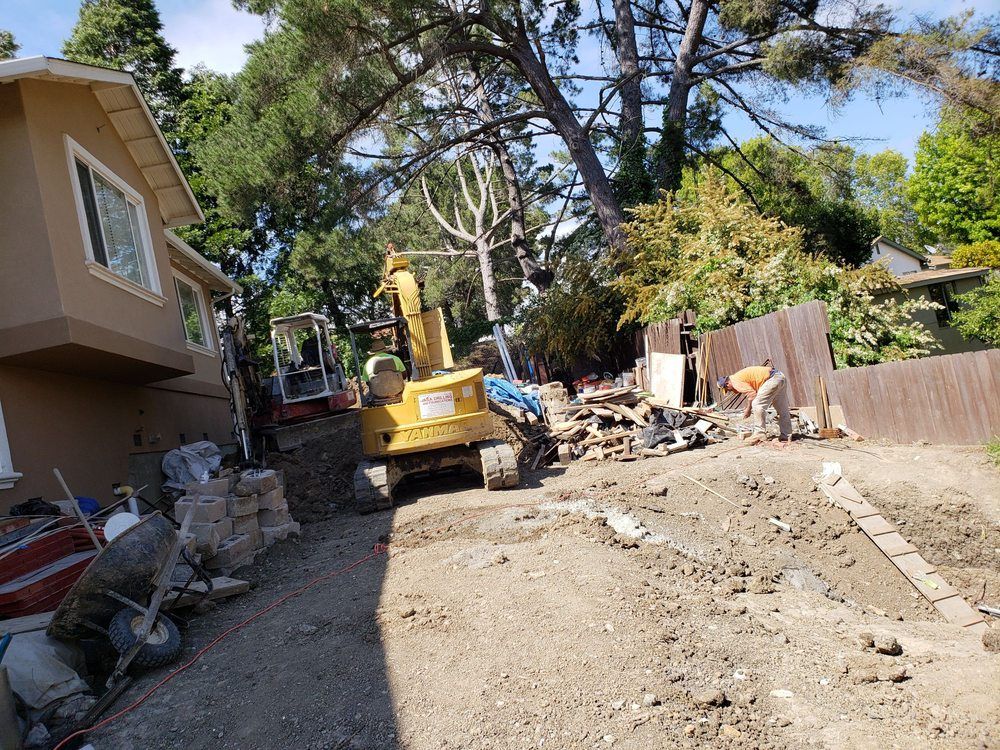 A yellow excavator is sitting in the dirt in front of a house.