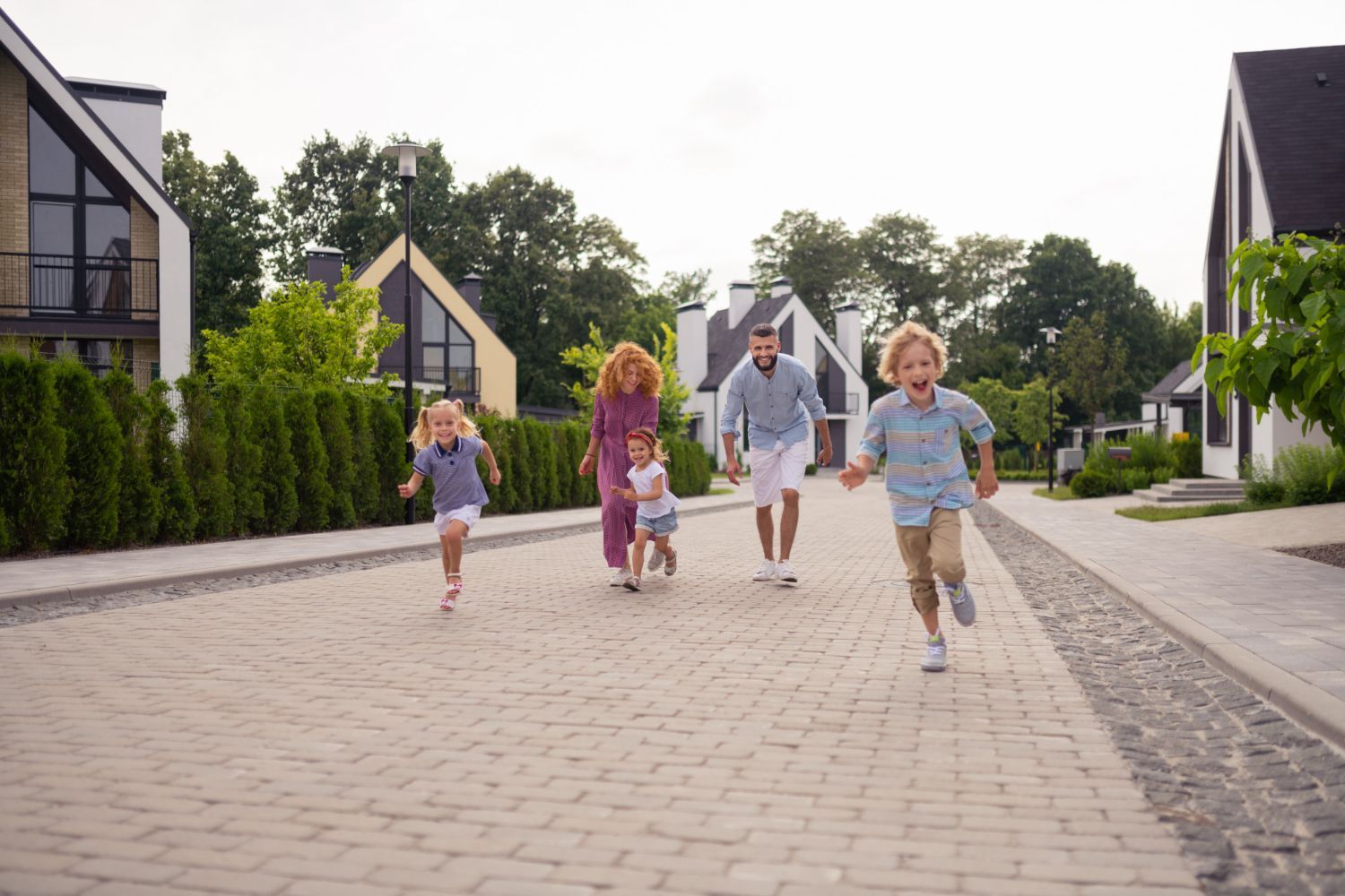 Family walking on a brick street in front of modern houses. Two children run ahead, parents follow.