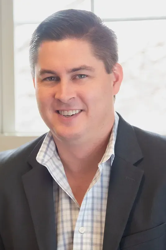 A man with a beard is wearing a white shirt and smiling for the camera.
