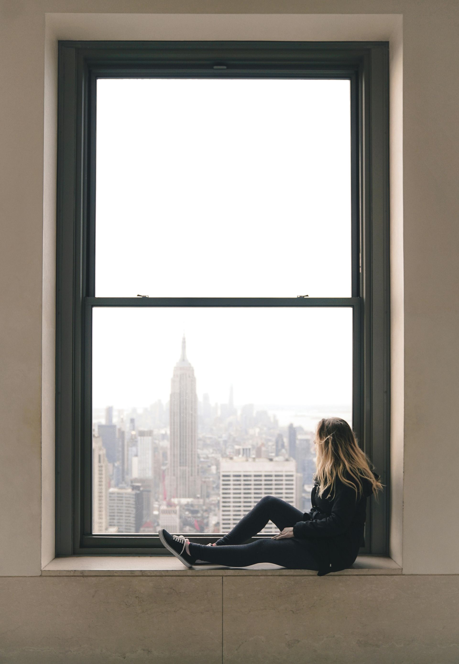 Woman sitting in a window, overlooking a city with the Empire State Building.