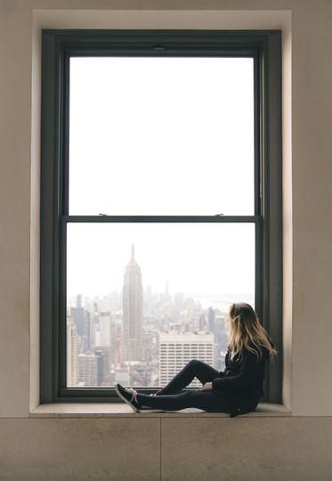 Woman sitting in a window, overlooking a city with the Empire State Building.