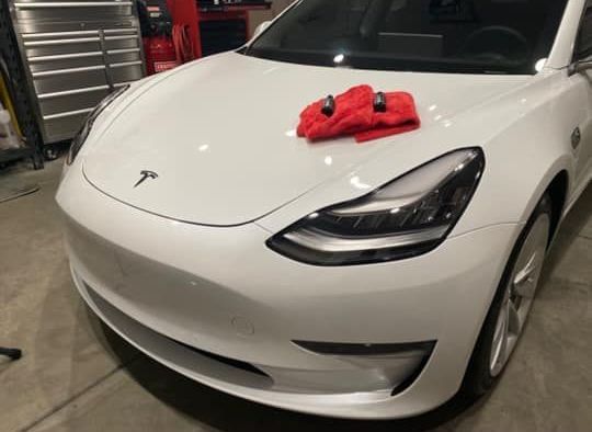 A white tesla model 3 with a red towel on the hood