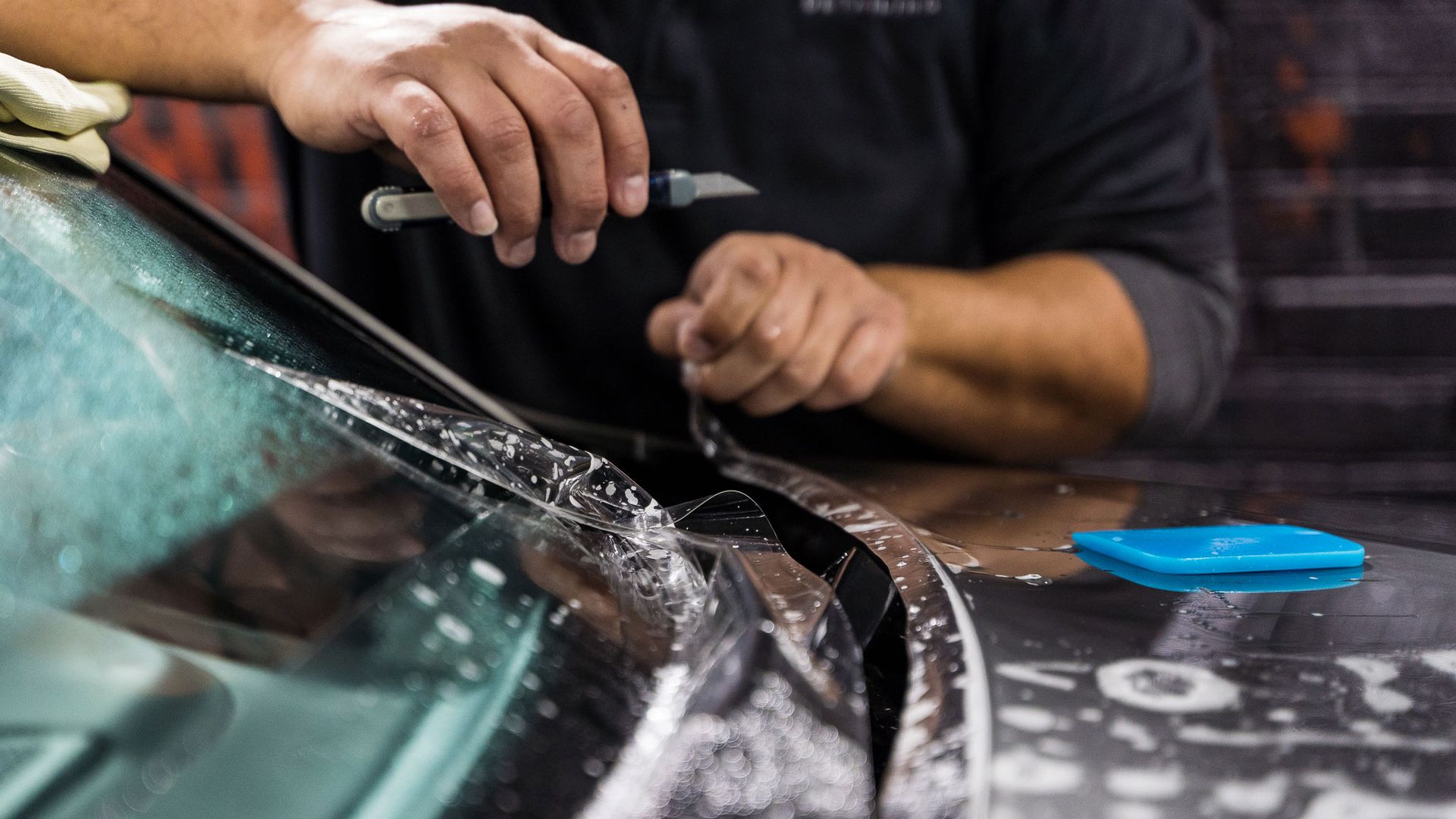 Person repairing a car windshield with a tool, with water spraying across the glass
