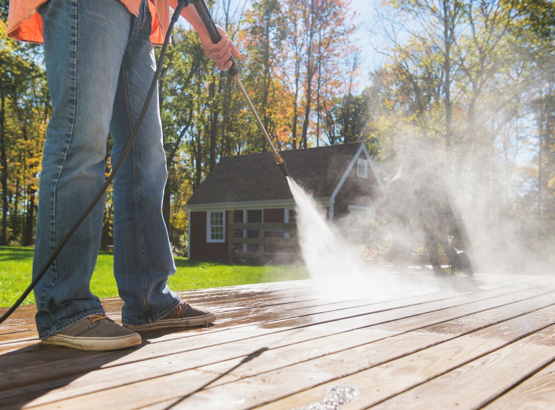 A man is using a high pressure washer to clean a wooden deck.