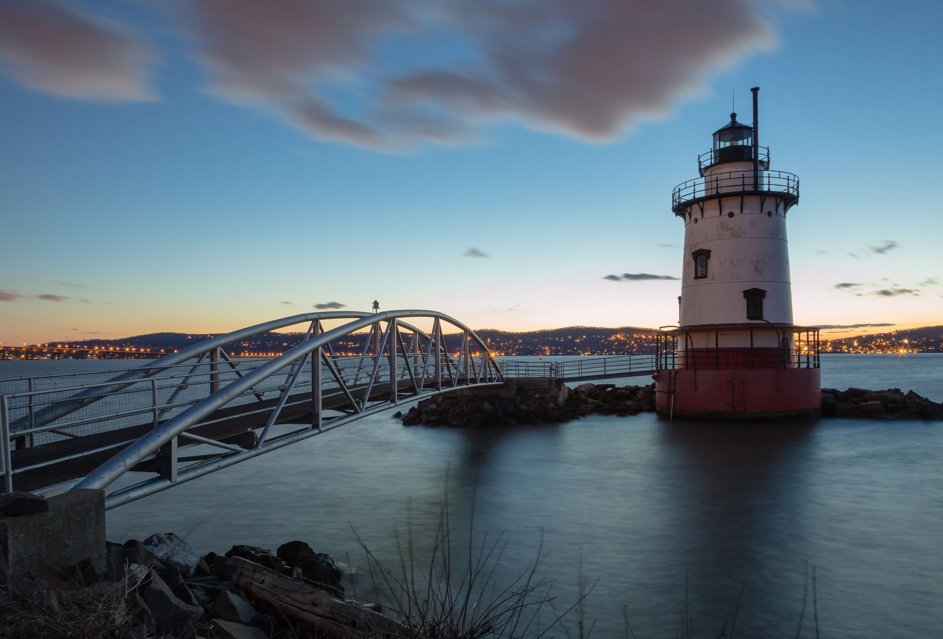 A lighthouse is in the middle of a body of water next to a bridge.