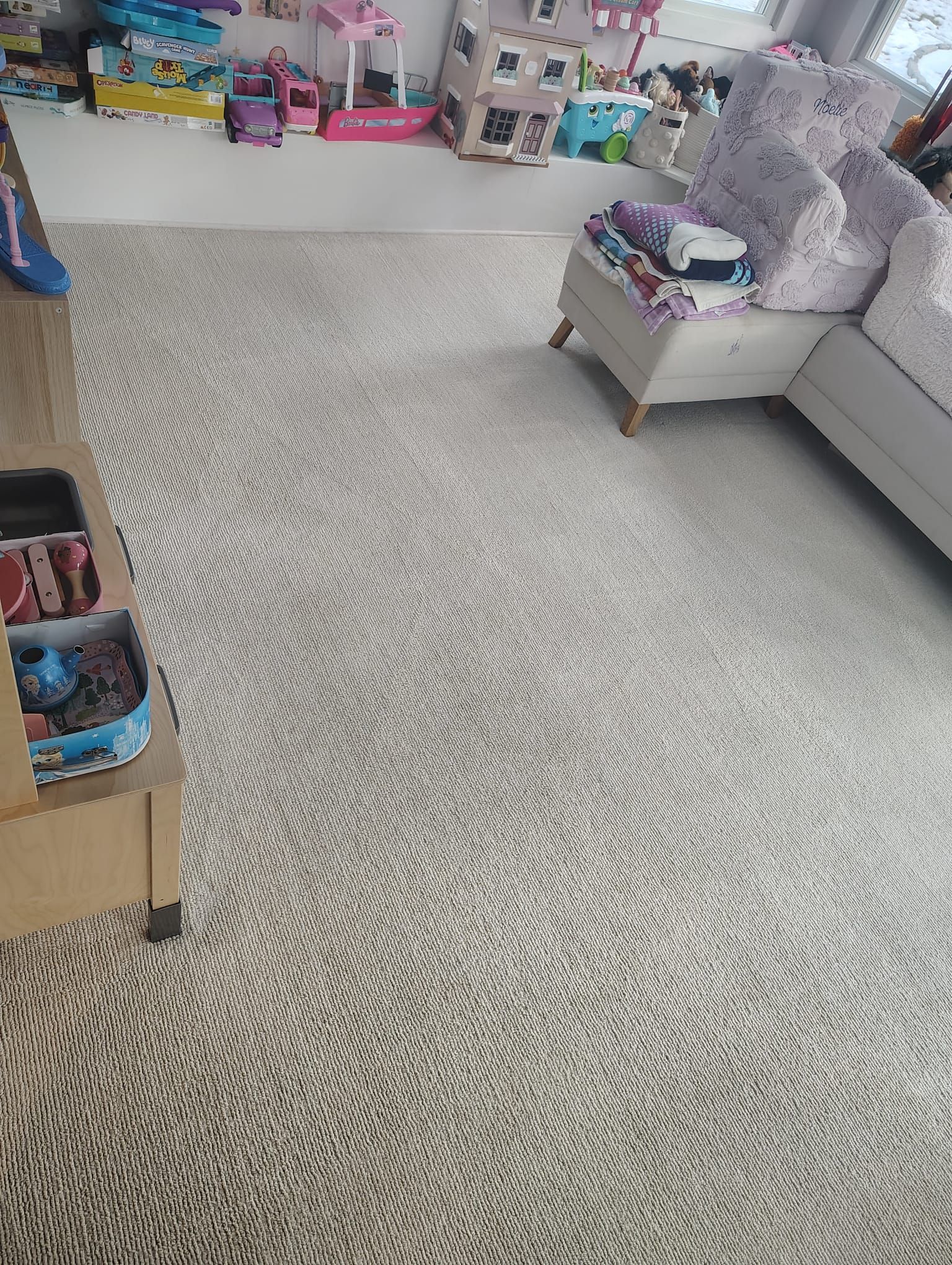 A beige carpeted room with toys displayed on a low shelf and an armchair with patterned fabric in the corner.