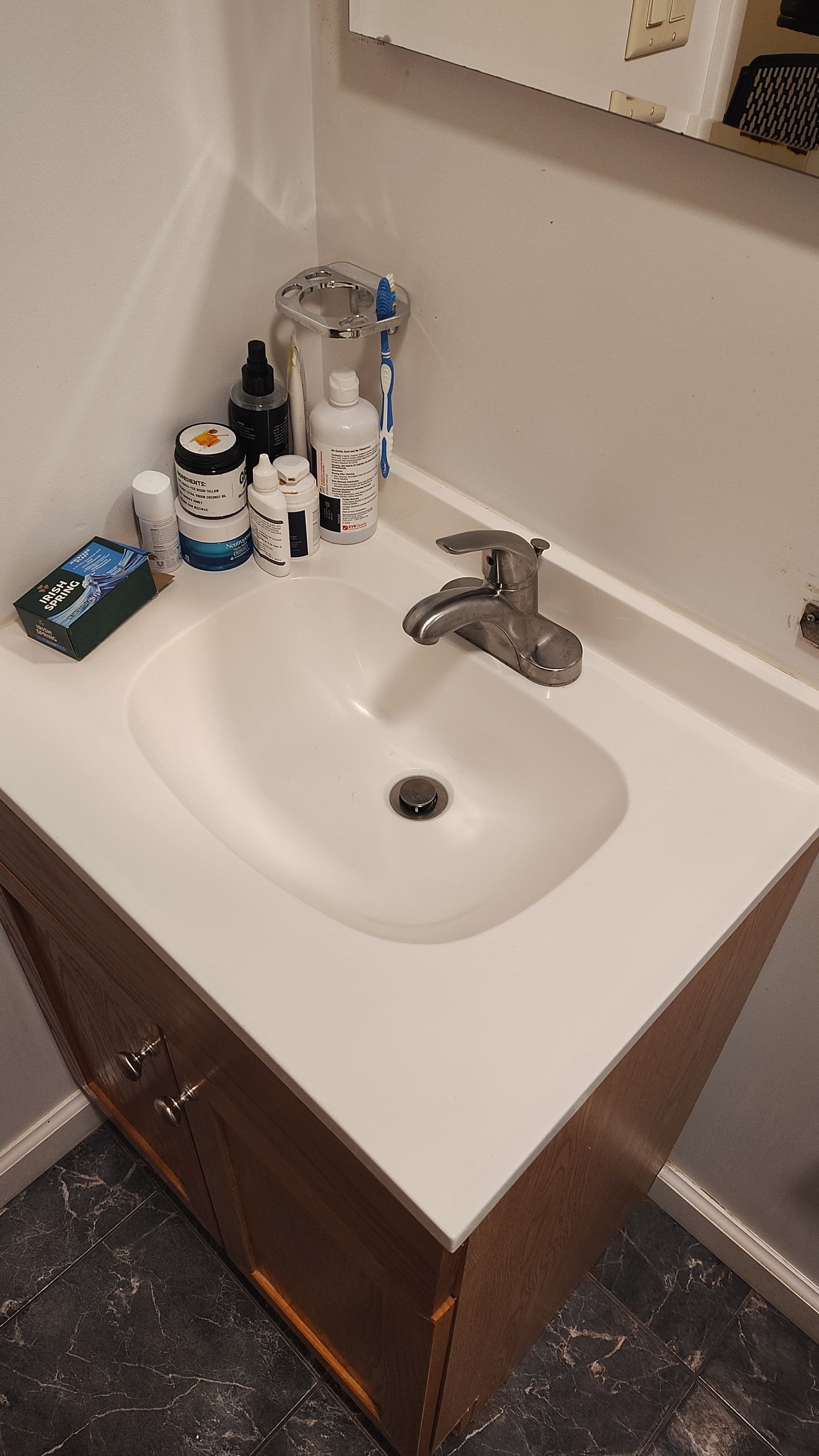 A bathroom vanity with a white sink, chrome faucet, and several toiletries arranged on the counter.