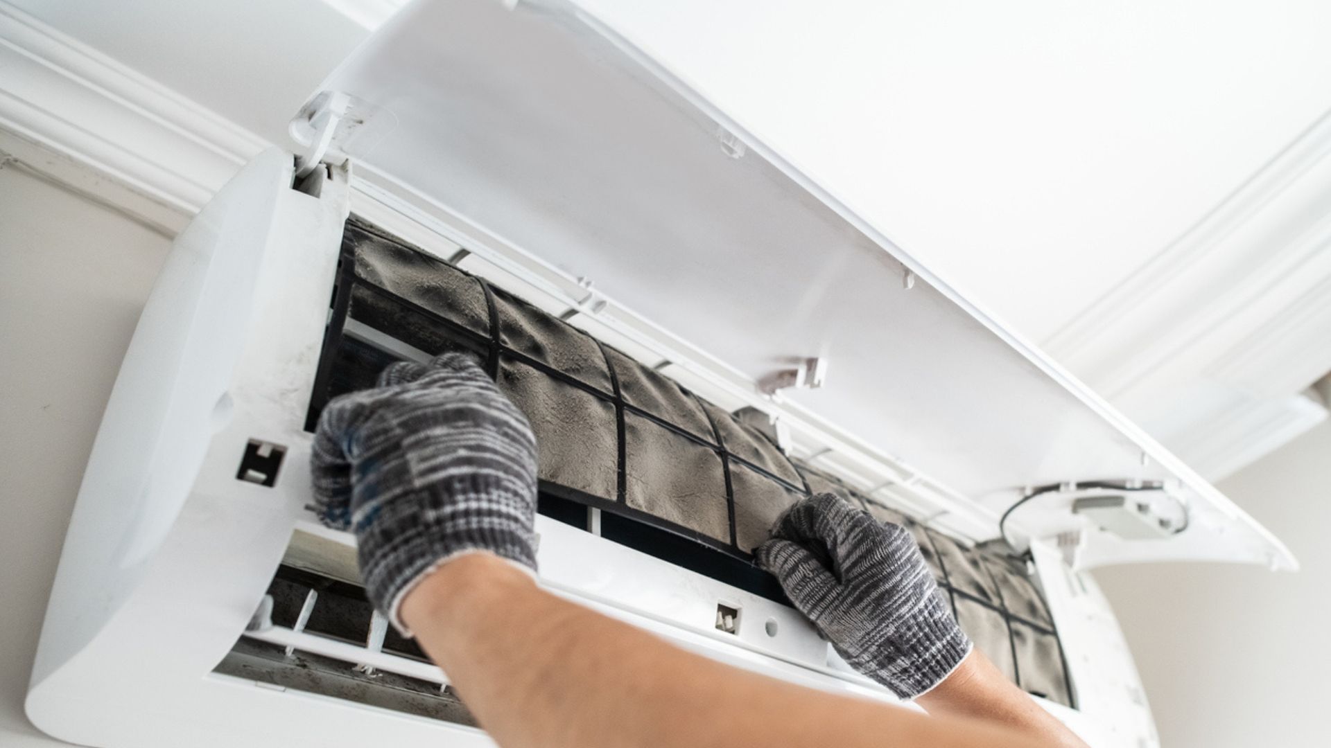 Gloved hands cleaning the filter inside a white wall-mounted air conditioner.
