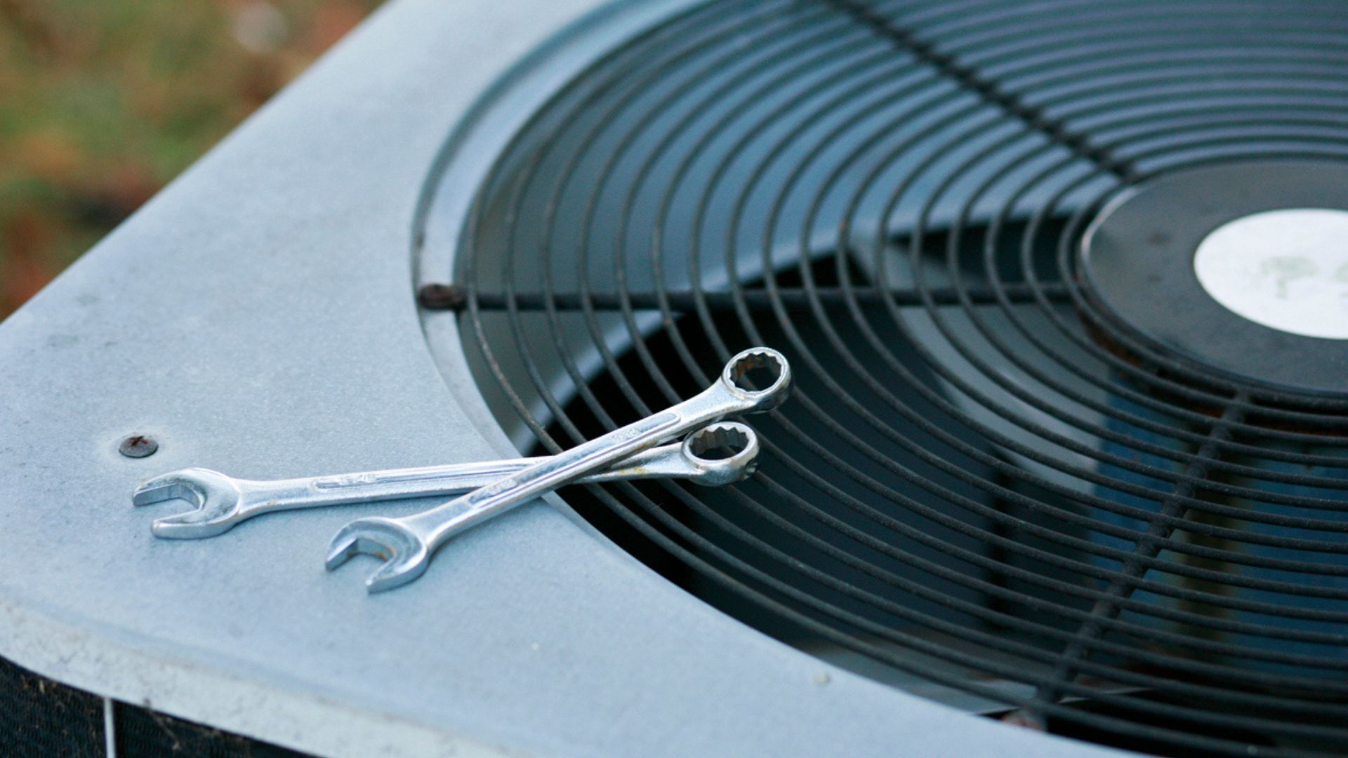 Two wrenches resting on the edge of an outdoor air conditioner fan grille
