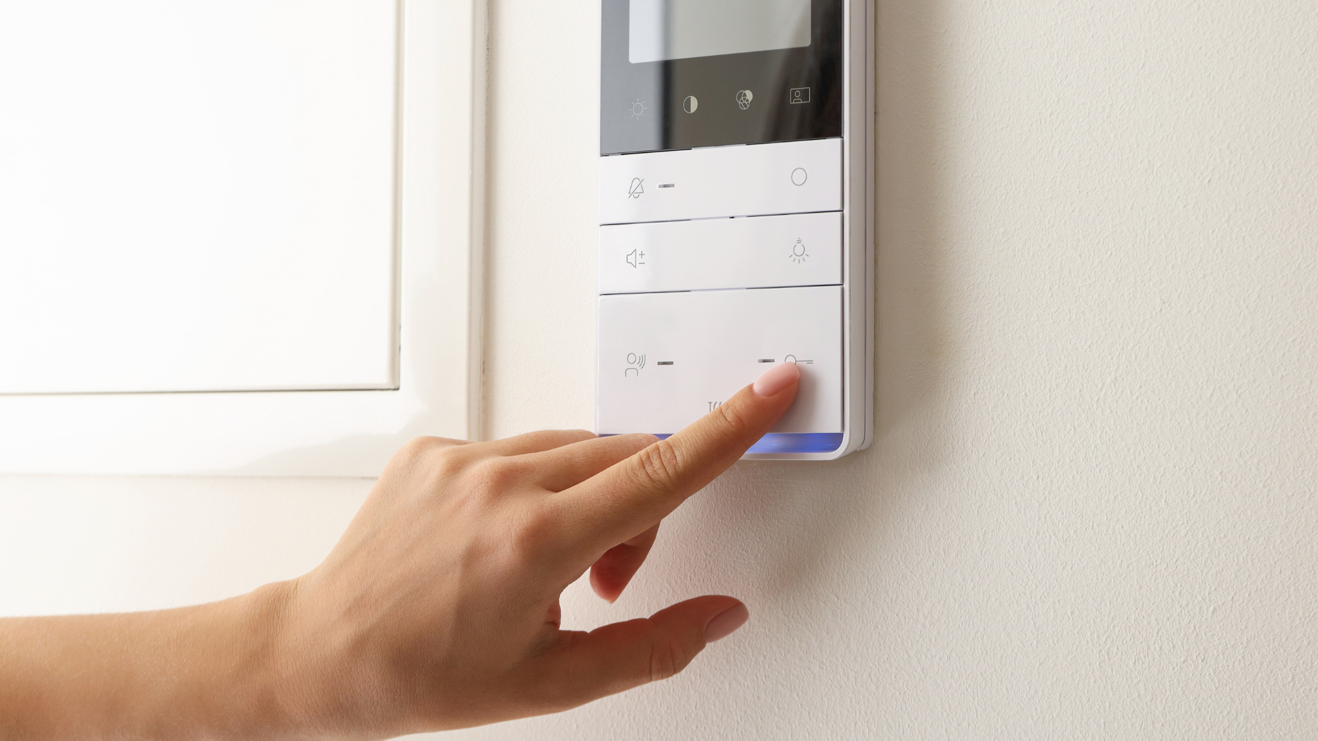 Hand pressing a wall-mounted touchscreen thermostat in a bright room