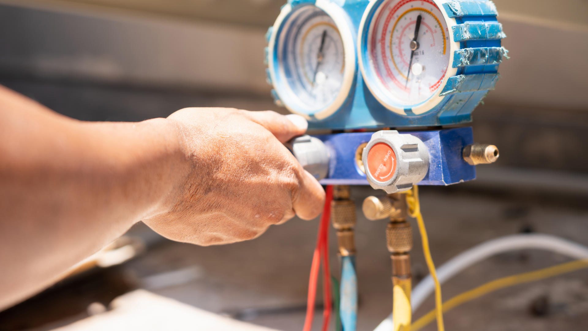 Hand holding a blue HVAC manifold gauge set with colored hoses and pressure dials.