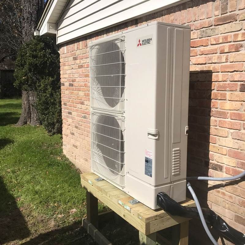 Mitsubishi heat pump unit on a wooden platform against a brick wall.