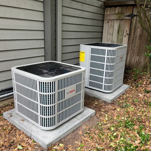 Two air conditioning units on concrete pads beside a building.