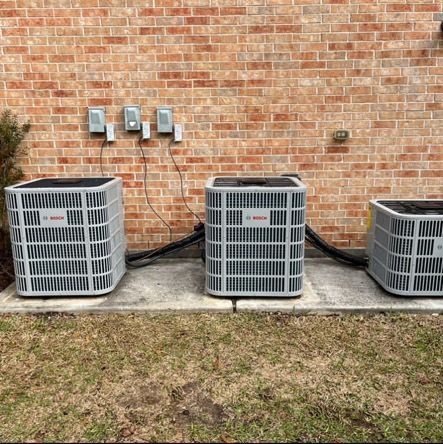 Three Bosch air conditioning units against a brick wall, electrical boxes above.