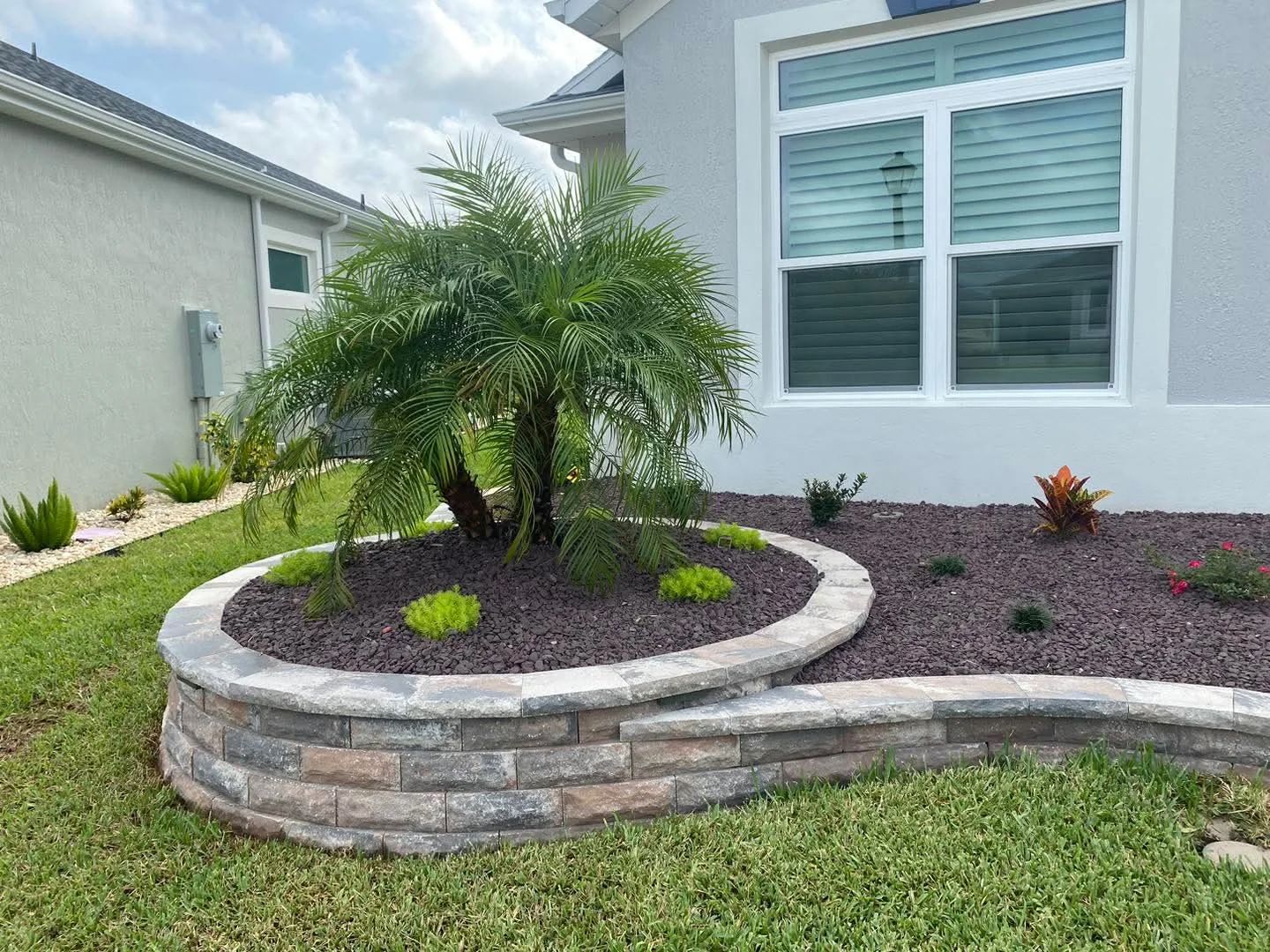 Curved brick retaining wall with landscaping and palm tree in front of a house.