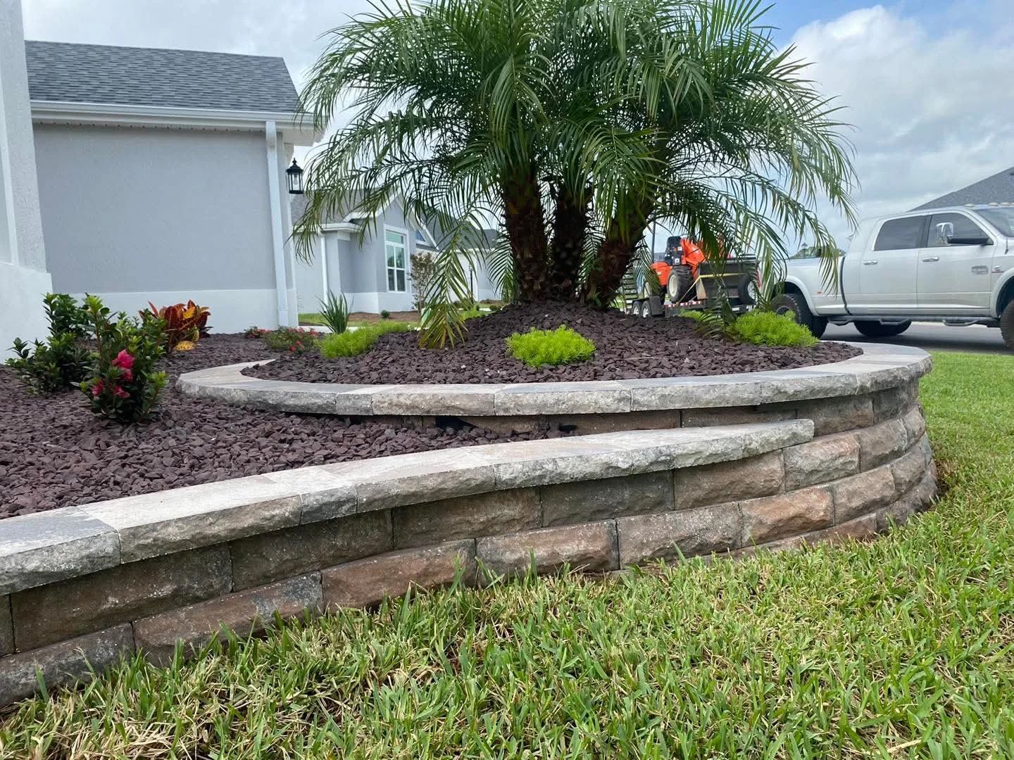 Stone tiered garden bed with palm tree and truck.
