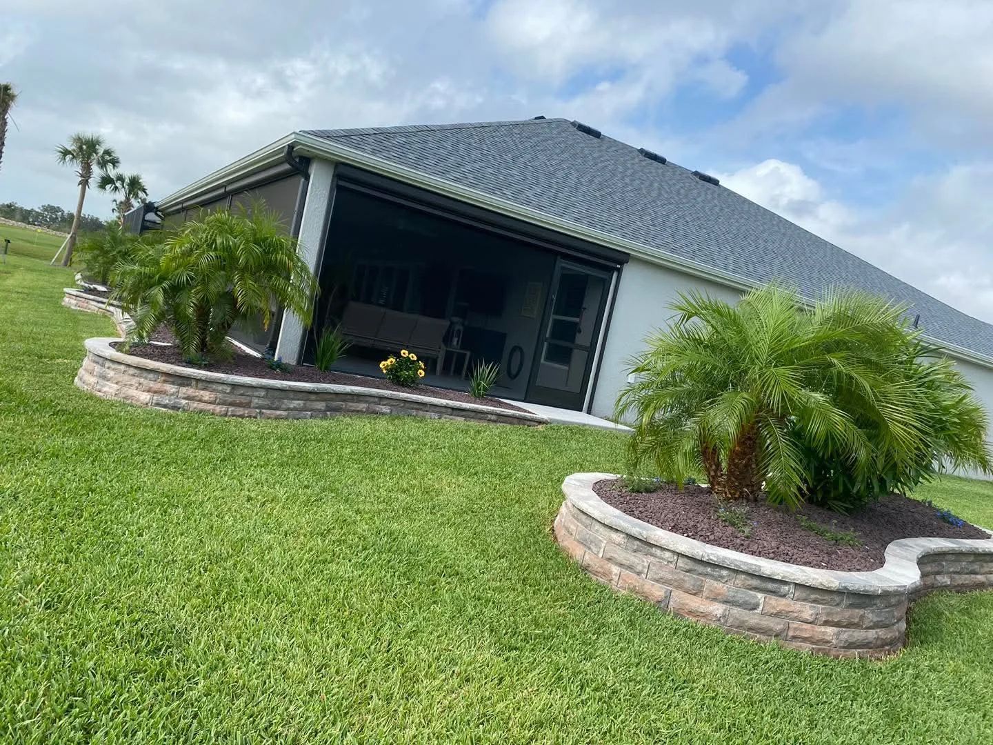 A house with a screened patio, surrounded by landscaped flower beds and green grass.