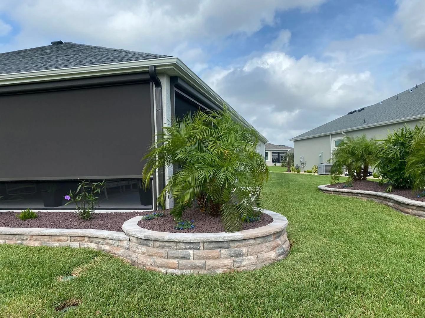 Backyard with a raised brick flowerbed, green lawn, and a home with a retractable screen.