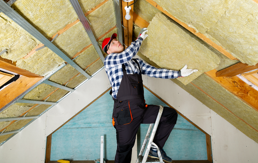 A man is standing on a ladder while installing insulation on the ceiling.