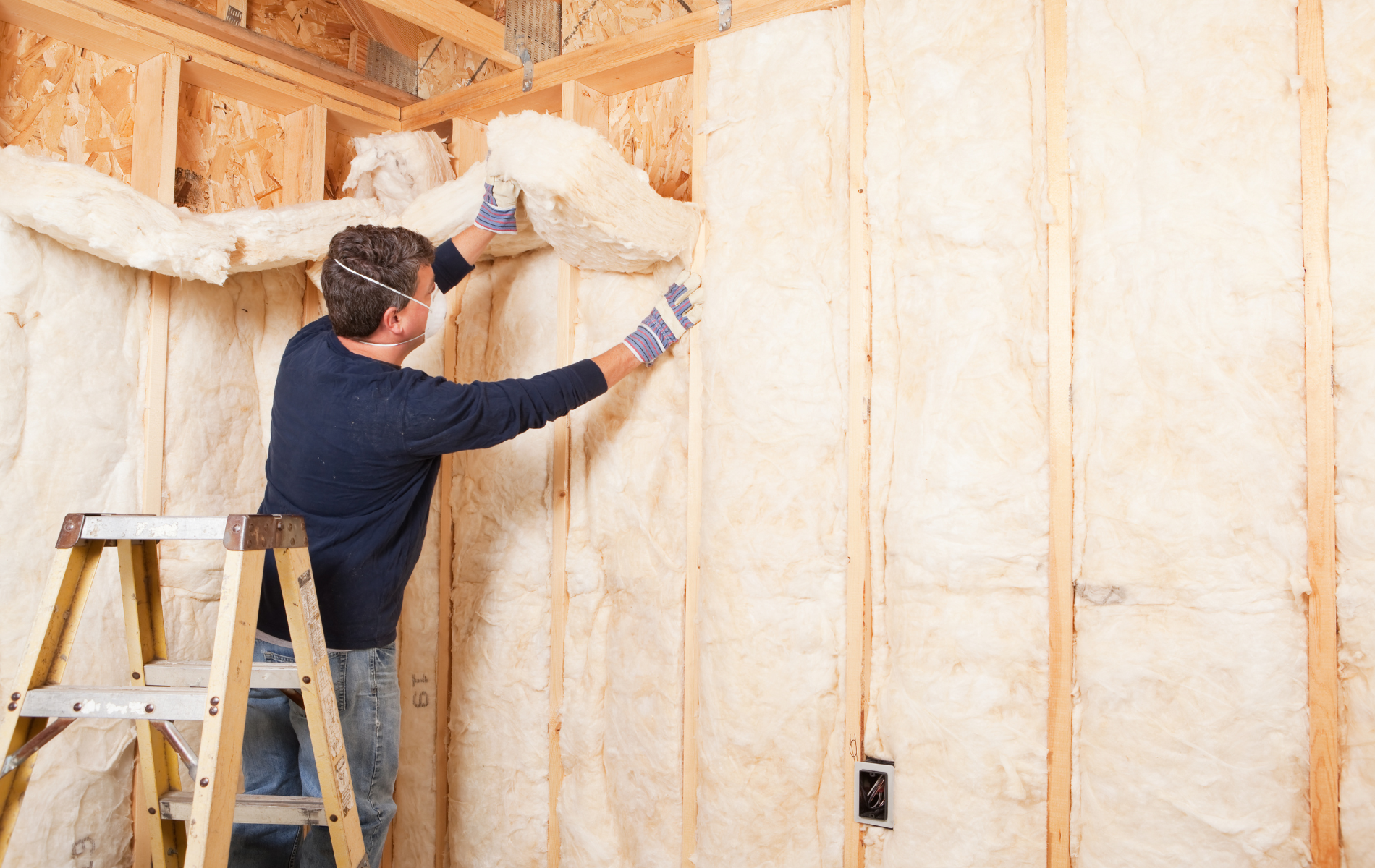 A man is standing on a ladder insulating a wall.